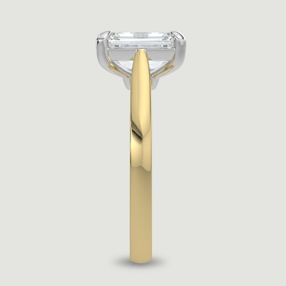An 18ct yellow gold single stone diamond engagement ring, set with a lab-grown emerald cut diamond held in a platinum four claw setting. Viewed from the edge.