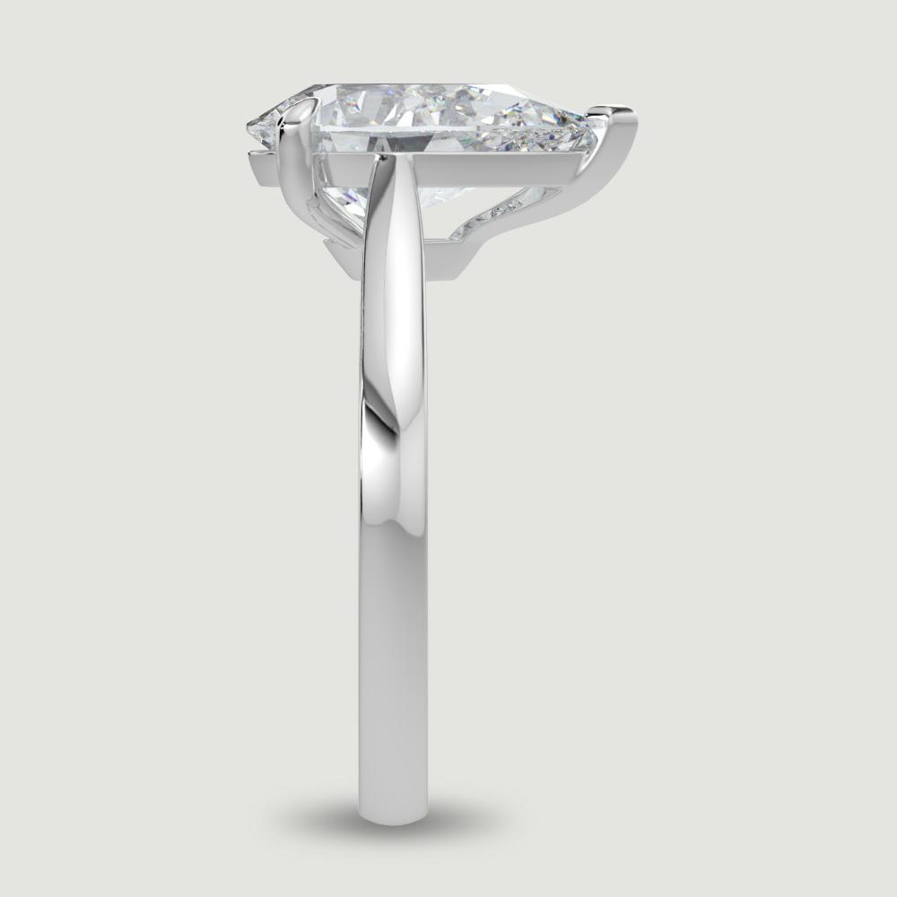 A platinum single stone diamond engagement ring, set with a lab-grown pear shape diamond held in a three claw setting. Viewed from the edge.