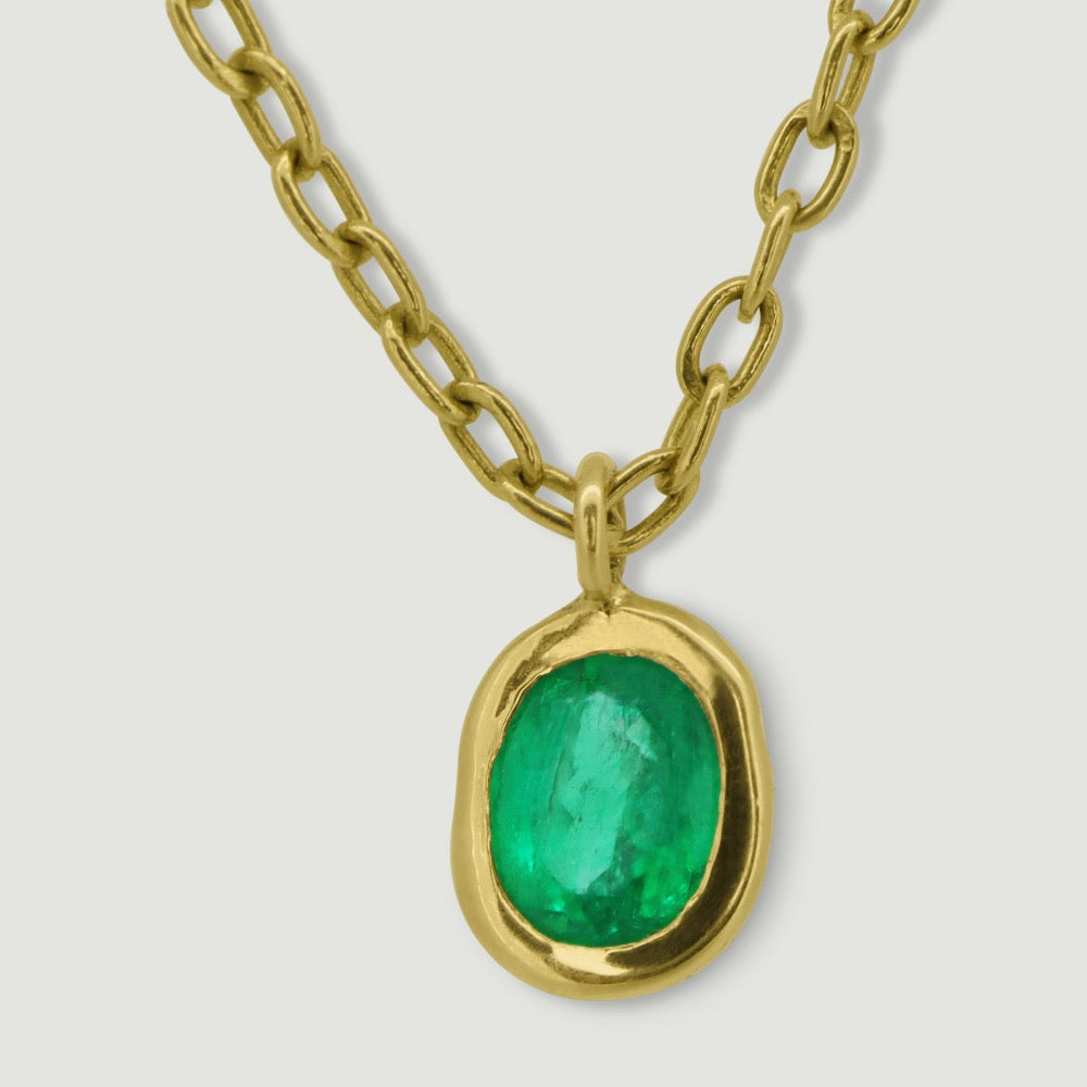 Yellow gold delicate bracelet with an oval charm rub over set with a single oval emerald - close-up of the emerald 2
