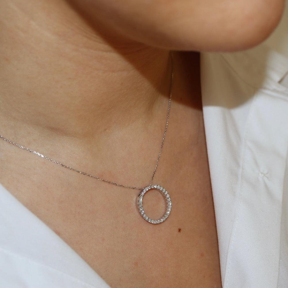 White gold diamond pendant, claw set with small round brilliant diamonds forming a circle 18mm in diameter, hanging on a fine chain - photographed on model