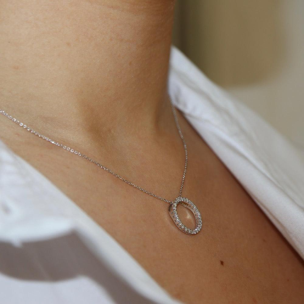 White gold diamond pendant, claw set with small round brilliant diamonds forming a circle 15mm in diameter, hanging on a fine chain -  photographed on model