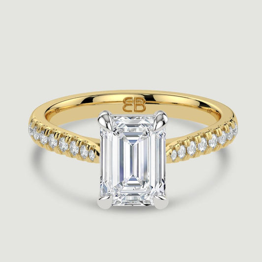 An 18ct yellow gold single stone diamond engagement ring, with micro-pavé set shoulders set with a lab-grown emerald cut diamond held in a platinum four claw setting. Viewed from above.
