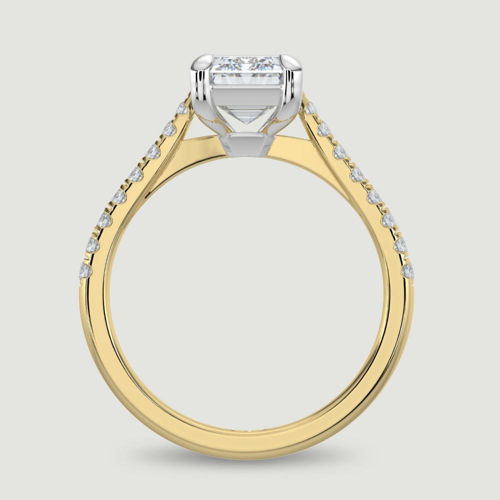 An 18ct yellow gold single stone diamond engagement ring, with micro-pavé set shoulders set with a lab-grown emerald cut diamond held in a platinum four claw setting. Viewed from the side.