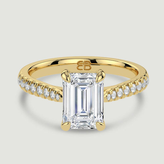 An 18ct yellow gold single stone diamond engagement ring, with micro-pavé set shoulders set with a lab-grown emerald cut diamond held in a four claw setting. Viewed from above.