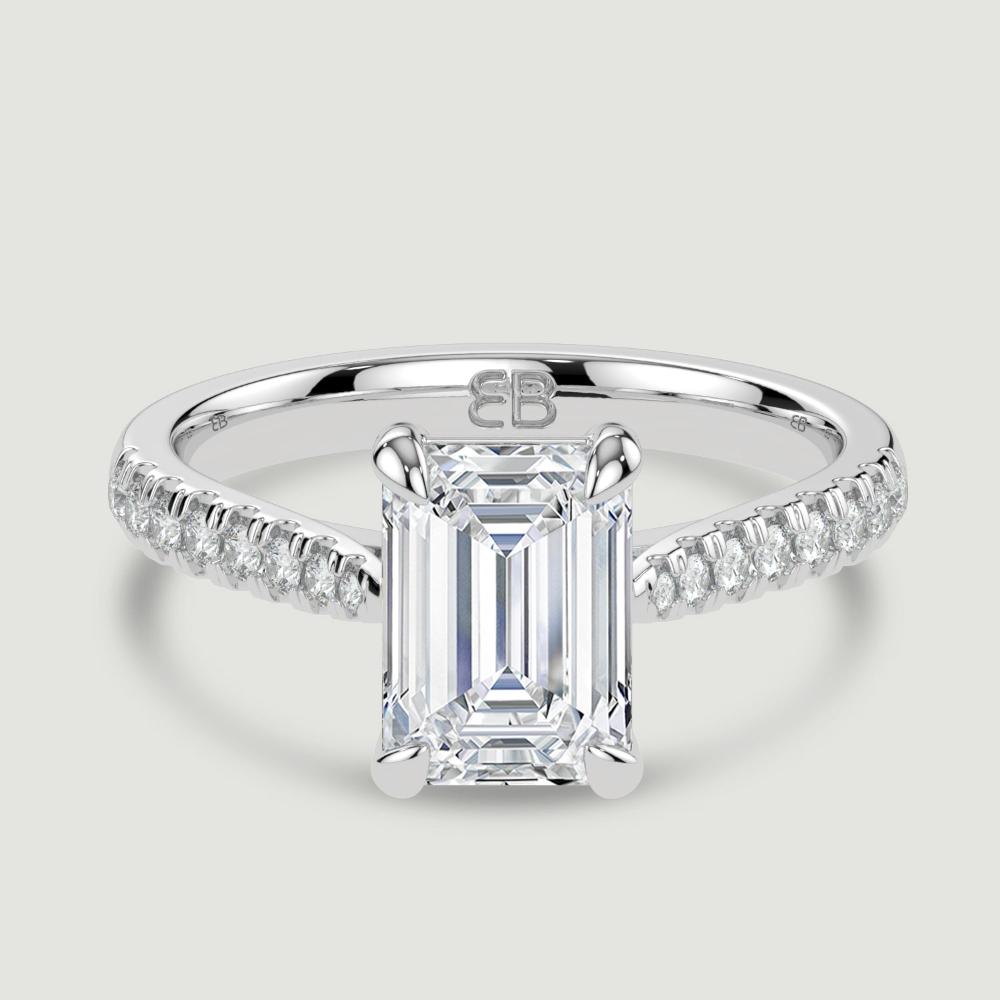A platinum single stone diamond engagement ring, with micro-pavé set shoulders set with a lab-grown emerald cut diamond held in a four claw setting. Viewed from above.