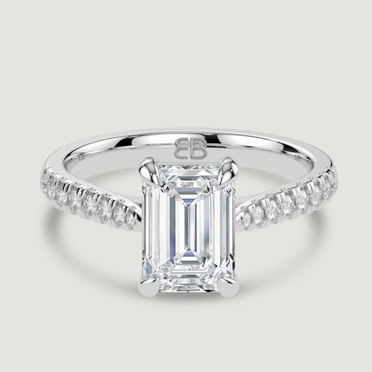 A platinum single stone diamond engagement ring, with micro-pavé set shoulders set with a lab-grown emerald cut diamond held in a four claw setting. Viewed from above.