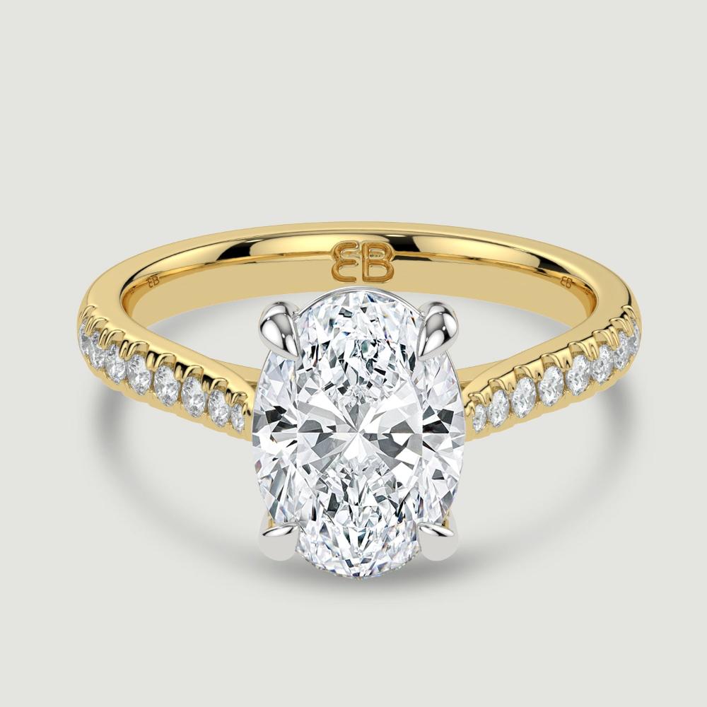 An 18ct yellow gold single stone diamond engagement ring, with micro-pavé set shoulders set with a lab-grown oval shape diamond held in a platinum four claw setting. Viewed from above.