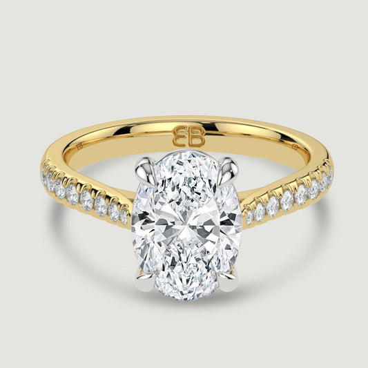 An 18ct yellow gold single stone diamond engagement ring, with micro-pavé set shoulders set with a lab-grown oval shape diamond held in a platinum four claw setting. Viewed from above.