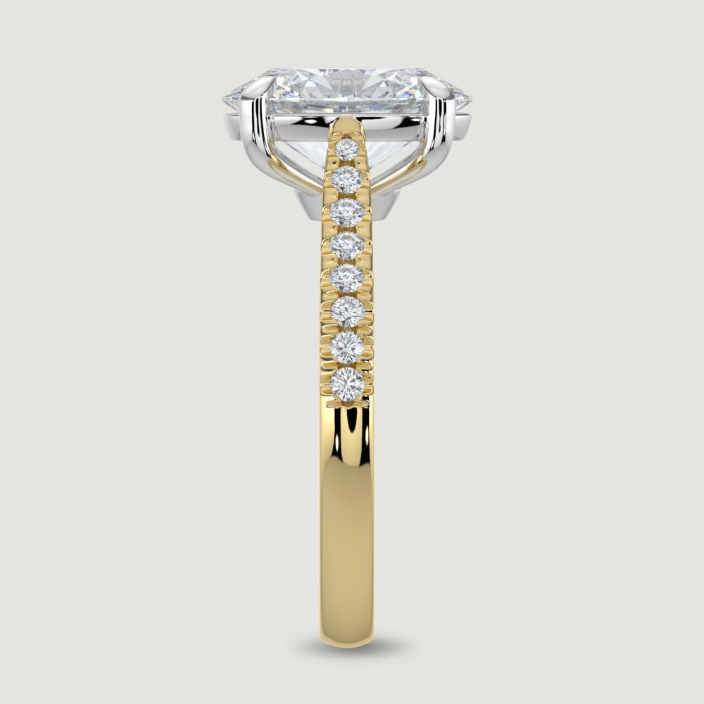 An 18ct yellow gold single stone diamond engagement ring, with micro-pavé set shoulders set with a lab-grown oval shape diamond held in a platinum four claw setting. Viewed from the edge.