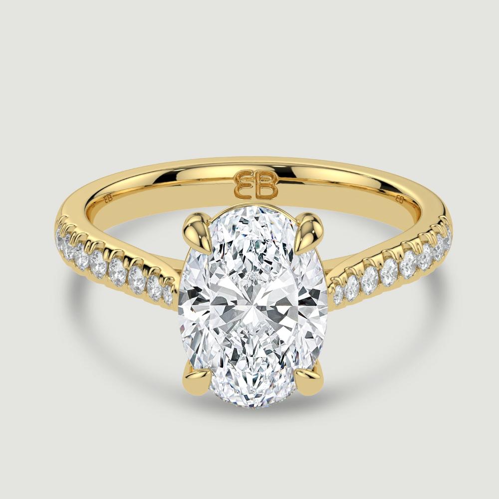 An 18ct yellow gold single stone diamond engagement ring, with micro-pavé set shoulders set with a lab-grown oval shape diamond held in a four claw setting. Viewed from above.