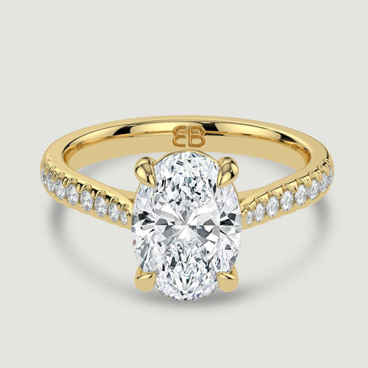An 18ct yellow gold single stone diamond engagement ring, with micro-pavé set shoulders set with a lab-grown oval shape diamond held in a four claw setting. Viewed from above.