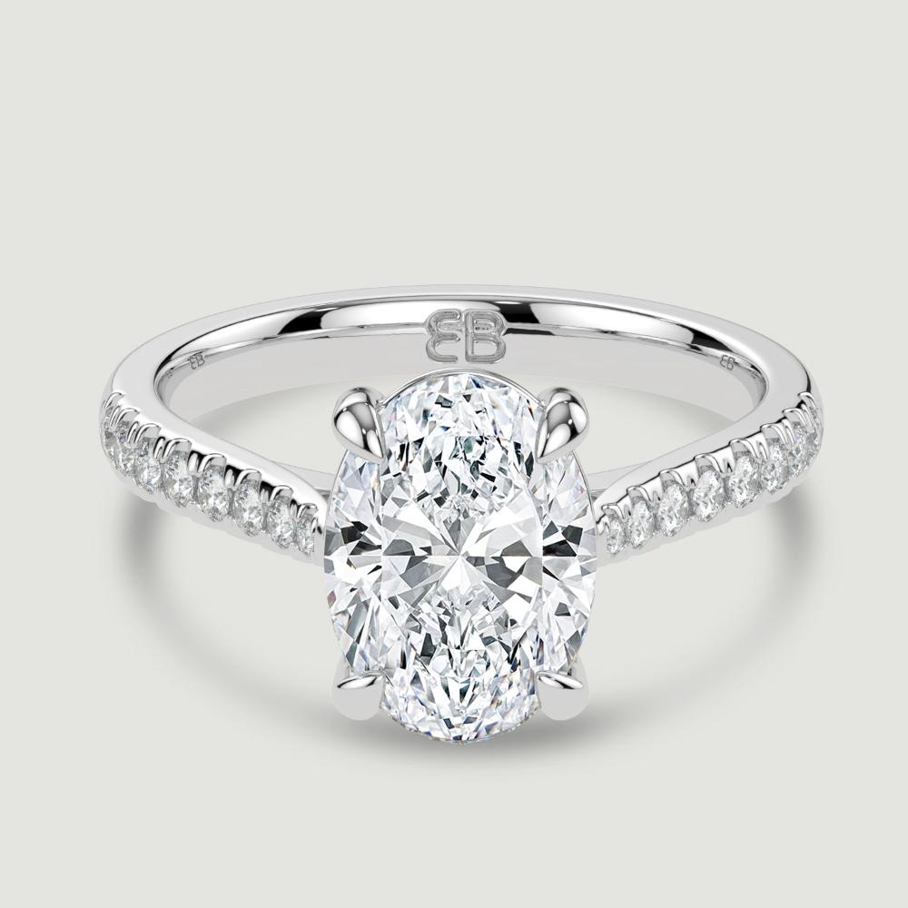 A platinum single stone diamond engagement ring, with micro-pavé set shoulders set with a lab-grown oval shape diamond held in a four claw setting. Viewed from above.