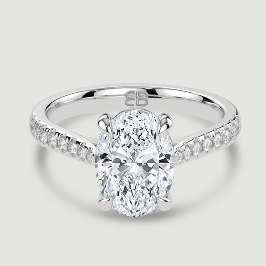 A platinum single stone diamond engagement ring, with micro-pavé set shoulders set with a lab-grown oval shape diamond held in a four claw setting. Viewed from above.