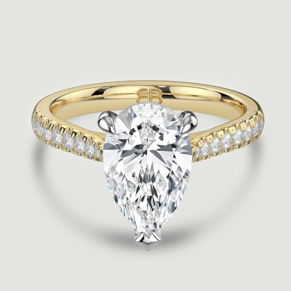 An 18ct yellow gold single stone diamond engagement ring, with micro-pavé set shoulders set with a lab-grown pear shape diamond held in a platinum three claw setting. Viewed from above.