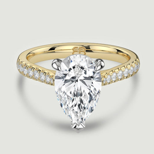 An 18ct yellow gold single stone diamond engagement ring, with micro-pavé set shoulders set with a lab-grown pear shape diamond held in a platinum three claw setting. Viewed from above.