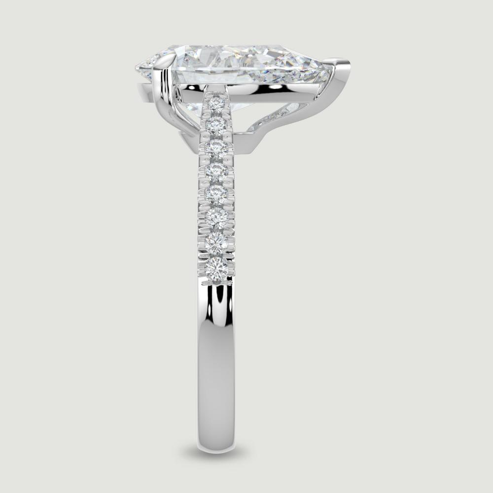 A platinum single stone diamond engagement ring, with micro-pavé set shoulders set with a lab-grown pear shape diamond held in a three claw setting. Viewed from the edge.