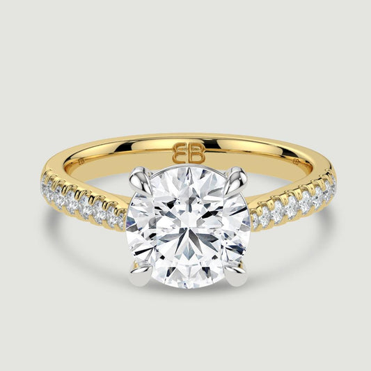 An 18ct yellow gold single stone diamond engagement ring, with micro-pavé set shoulders set with a lab-grown round brilliant diamond held in a platinum four claw setting. Viewed from above.