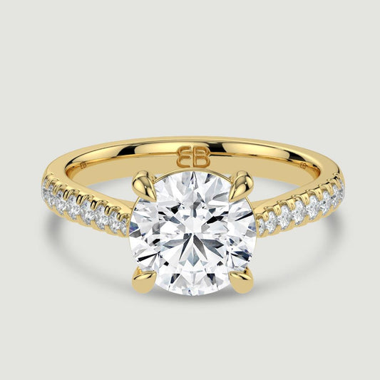 An 18ct yellow gold single stone diamond engagement ring, with micro-pavé set shoulders set with a lab-grown round brilliant diamond held in a four claw setting. Viewed from above.
