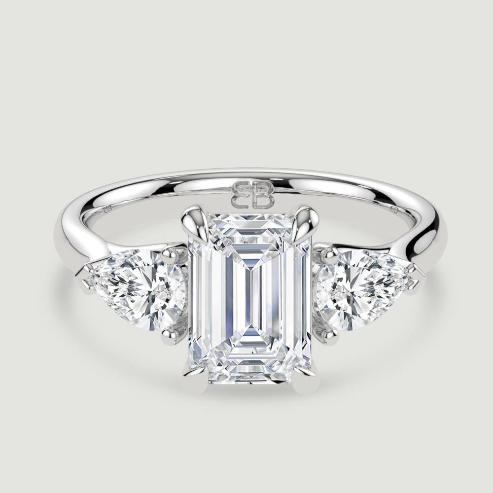 A platinum three stone diamond engagement ring, set with a lab-grown emerald cut diamond centre stone held in a four claw setting flanked by a pear shaped lab-grown diamond on either side, held in three claws. Viewed from above.