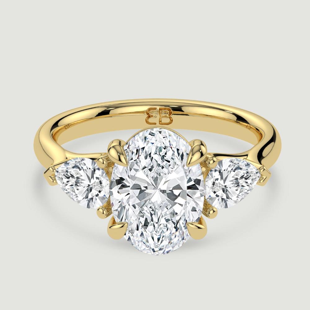 An 18ct yellow gold three stone diamond engagement ring, set with a lab-grown oval shape diamond centre stone held in a four claw setting flanked by a pear shaped lab-grown diamond on either side, held in three claws. Viewed from above.