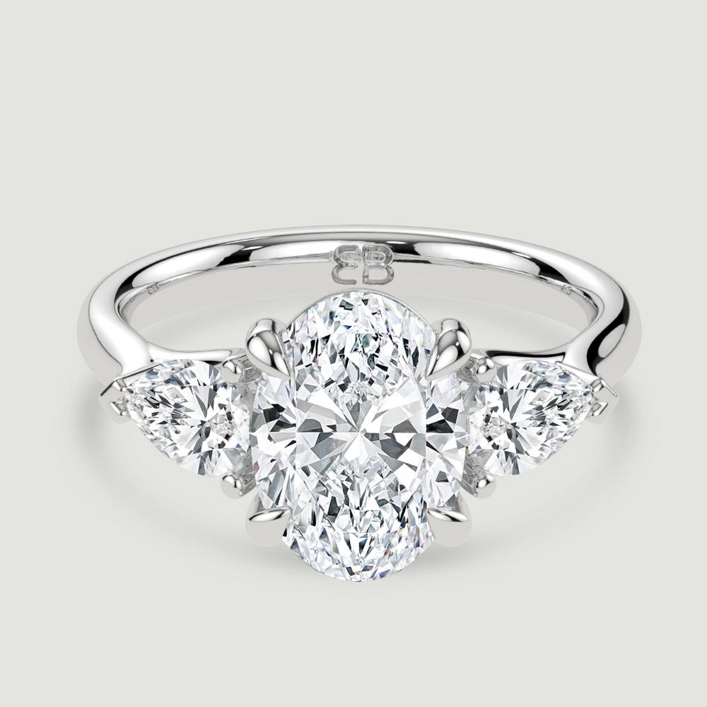 A platinum three stone diamond engagement ring, set with a lab-grown oval shape diamond centre stone held in a four claw setting flanked by a pear shaped lab-grown diamond on either side, held in three claws. Viewed from above.