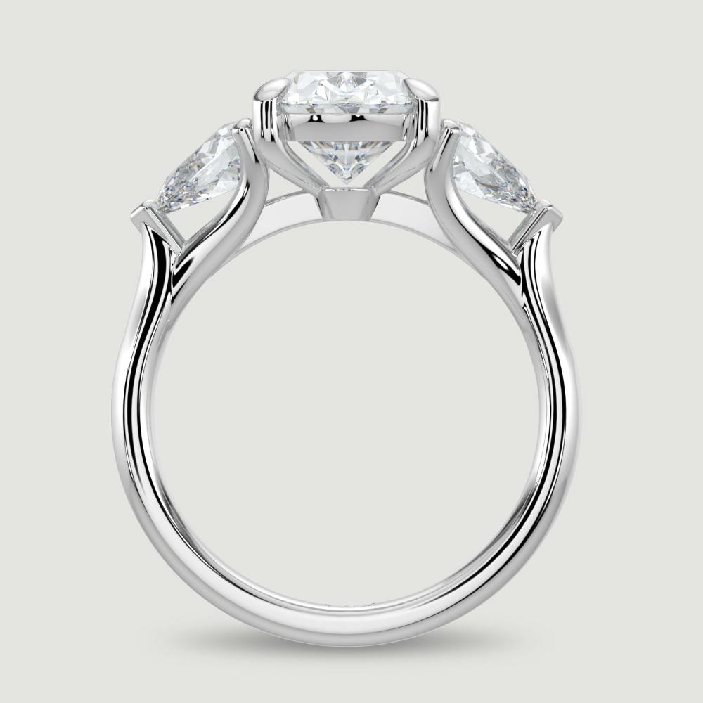 A platinum three stone diamond engagement ring, set with a lab-grown oval shape diamond centre stone held in a four claw setting flanked by a pear shaped lab-grown diamond on either side, held in three claws. Viewed from the side.