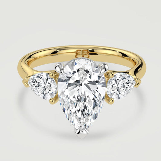 An 18ct yellow gold three stone diamond engagement ring, set with a lab-grown pear shape diamond centre stone held in a platinum three claw setting flanked by a pear shaped lab-grown diamond on either side, held in three claws. Viewed from above.