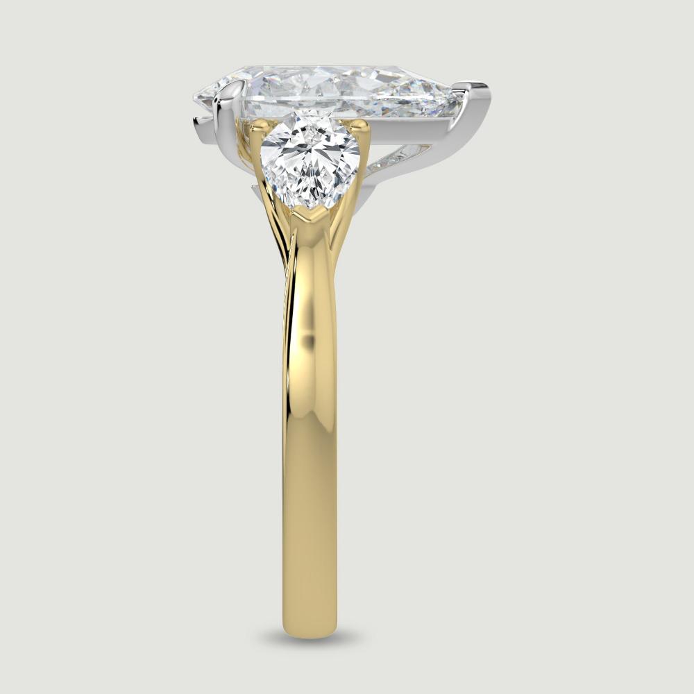 An 18ct yellow gold three stone diamond engagement ring, set with a lab-grown pear shape diamond centre stone held in a platinum three claw setting flanked by a pear shaped lab-grown diamond on either side, held in three claws. Viewed from the edge.