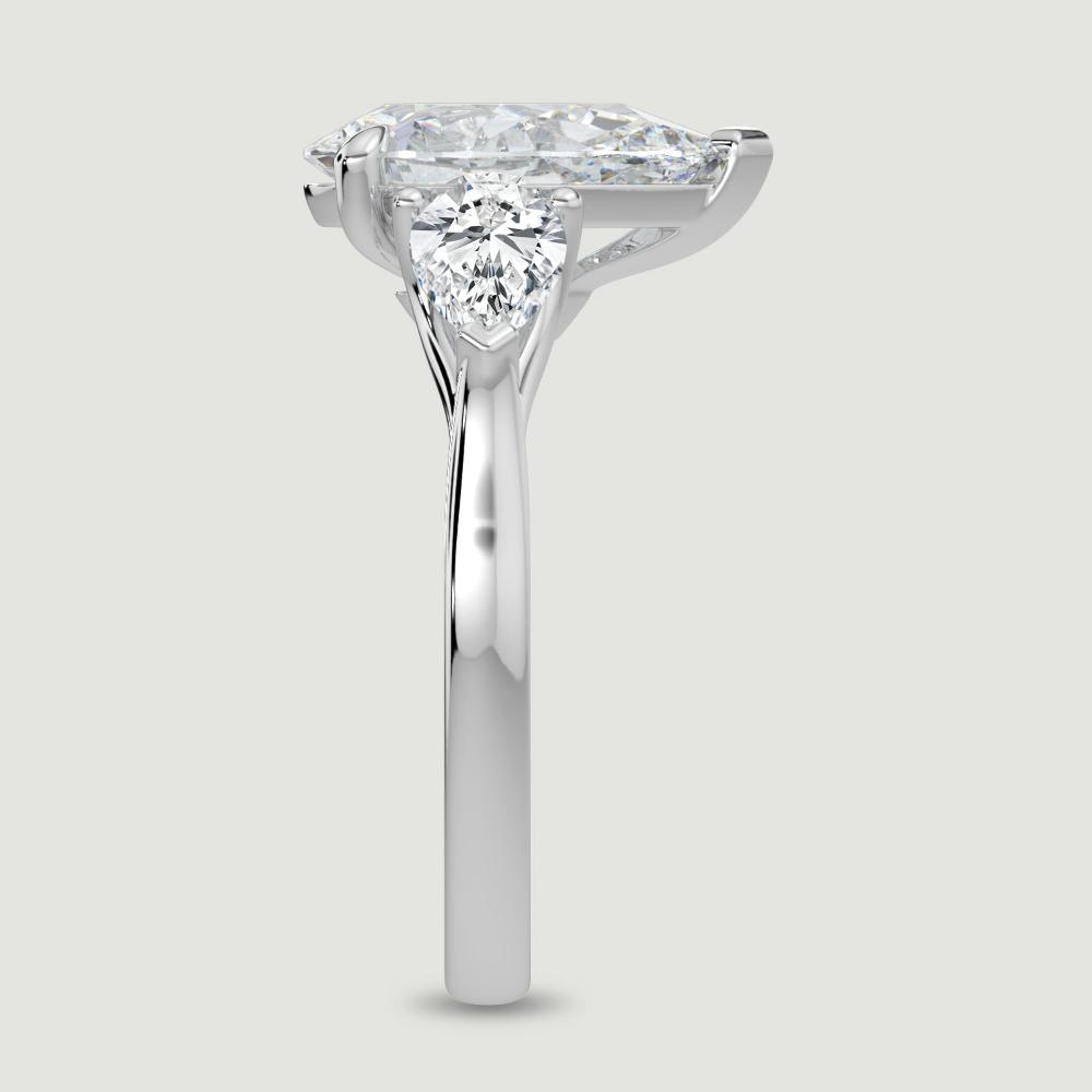 A platinum three stone diamond engagement ring, set with a lab-grown pear shape diamond centre stone held in a three claw setting flanked by a pear shaped lab-grown diamond on either side, held in three claws. Viewed from the edge.