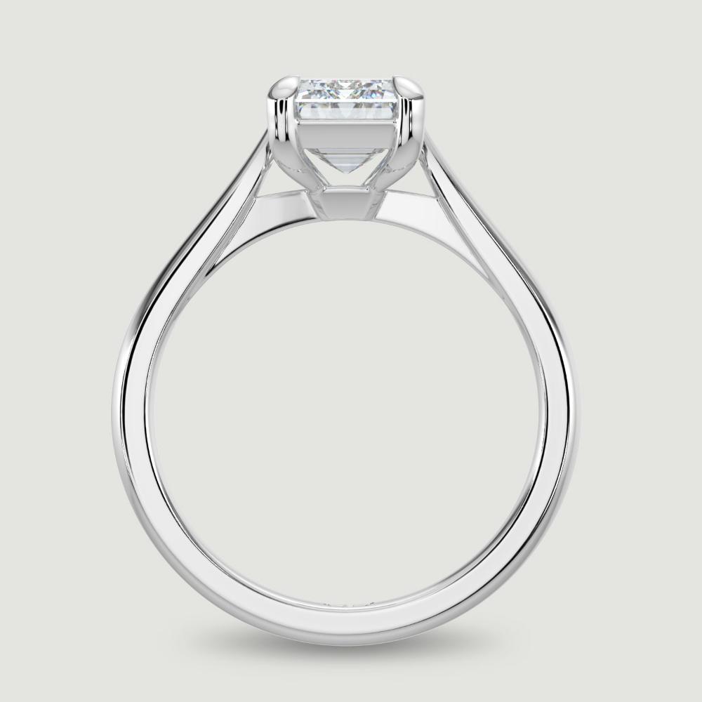 A platinum single stone diamond engagement ring, set with a lab-grown emerald cut diamond held in a four claw setting. Viewed from the side.
