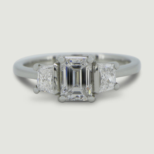 Platinum trilogy diamond ring with an emerald cut centre stone with a trapez cut diamond set on either side - view from the top