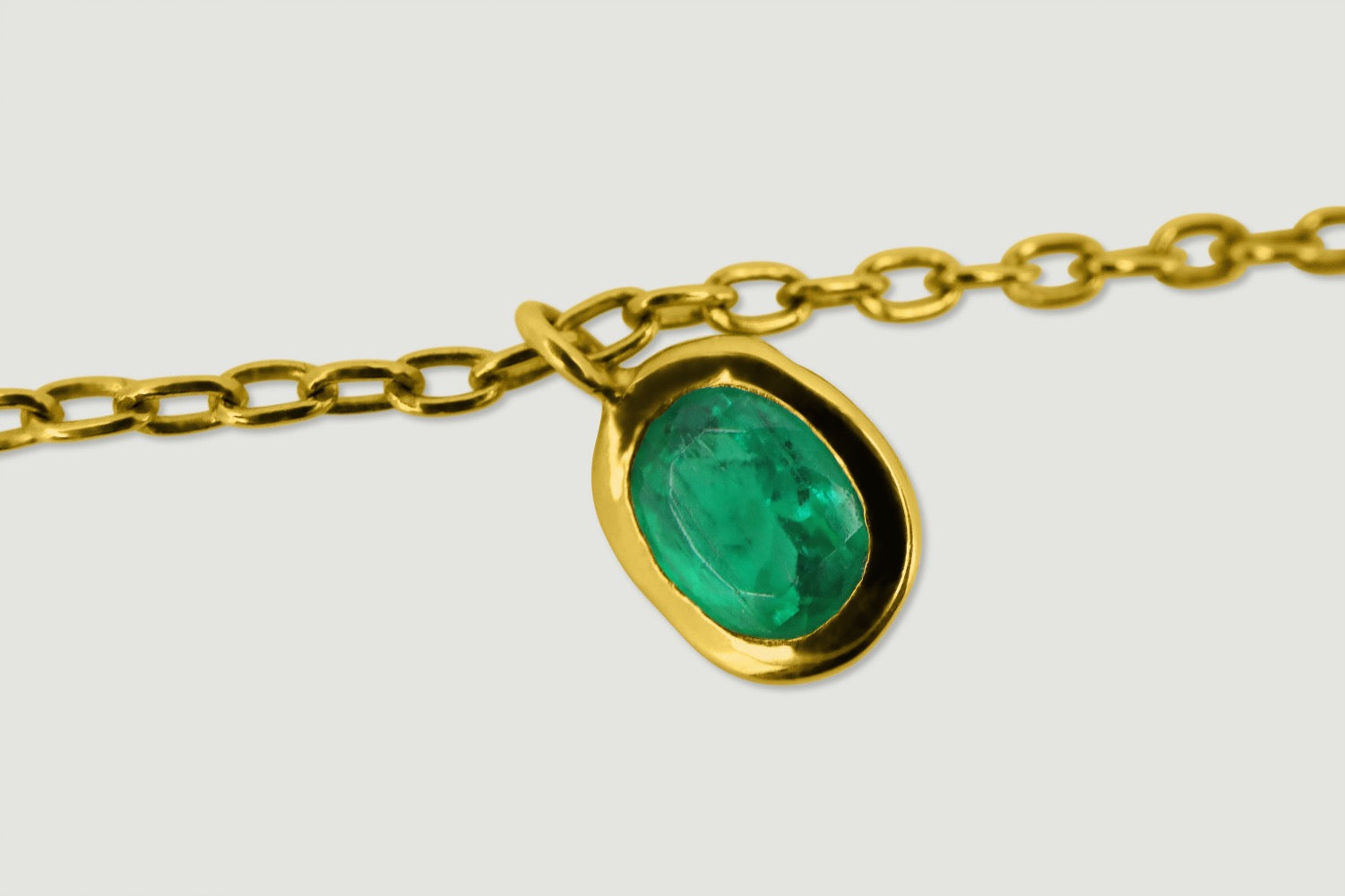 Yellow gold delicate bracelet with an oval charm rub over set with a single oval emerald - close-up of the emerald 1