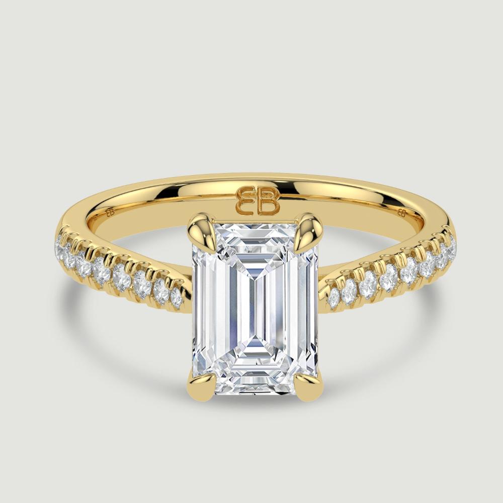 An 18ct yellow gold single stone diamond engagement ring, with micro-pavé set shoulders set with a lab-grown emerald cut diamond held in a four claw setting. Viewed from above.
