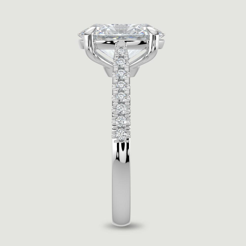 A platinum single stone diamond engagement ring, with micro-pavé set shoulders set with a lab-grown oval shape diamond held in a four claw setting. Viewed from the edge.
