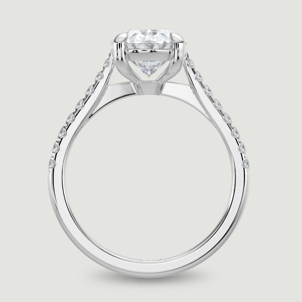 A platinum single stone diamond engagement ring, with micro-pavé set shoulders set with a lab-grown oval shape diamond held in a four claw setting. Viewed from the side.