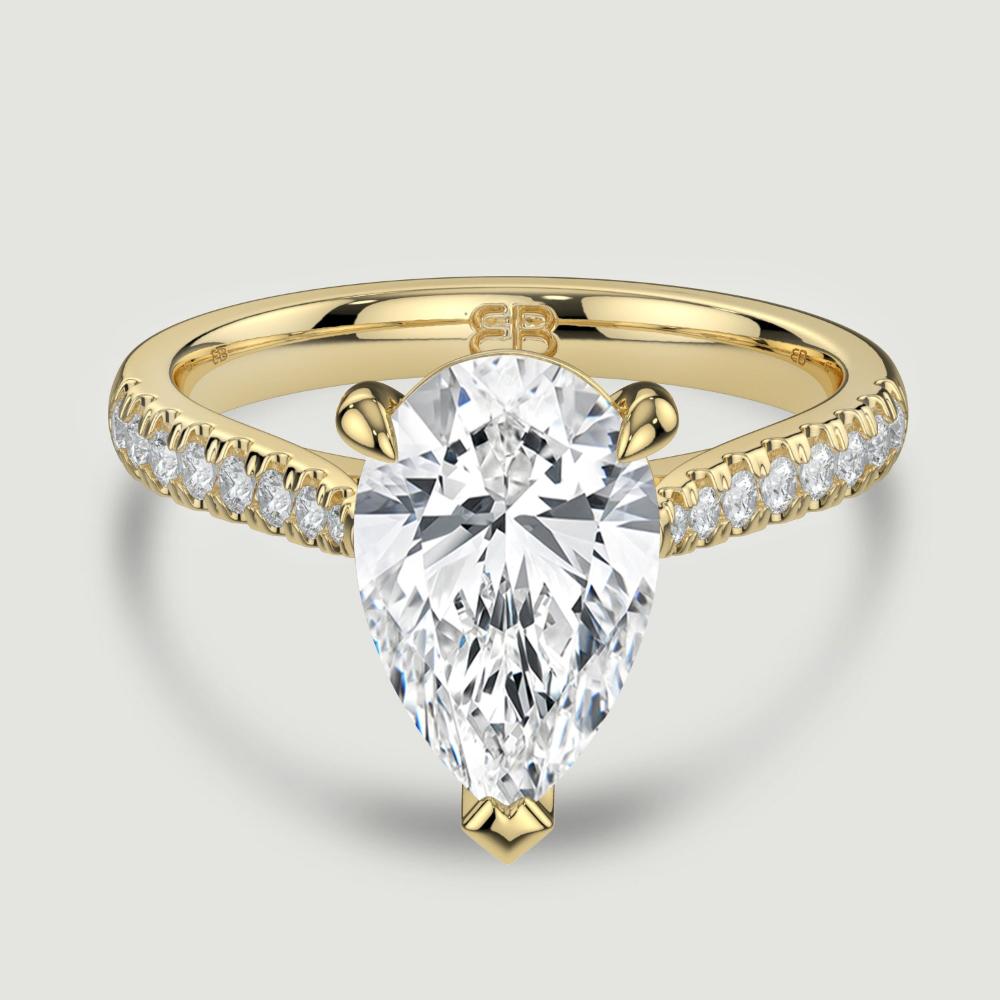 An 18ct yellow gold single stone diamond engagement ring, with micro-pavé set shoulders set with a lab-grown pear shape diamond held in a three claw setting. Viewed from above.