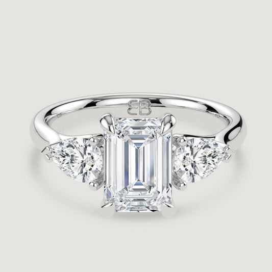 A platinum three stone diamond engagement ring, set with a lab-grown emerald cut diamond centre stone held in a four claw setting flanked by a pear shaped lab-grown diamond on either side, held in three claws. Viewed from above.
