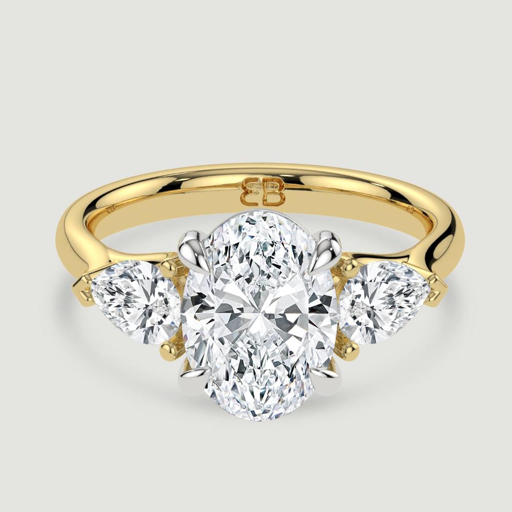 An 18ct yellow gold three stone diamond engagement ring, set with a lab-grown oval shape diamond centre stone held in a platinum four claw setting flanked by a pear shaped lab-grown diamond on either side, held in three claws. Viewed from above.