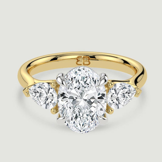 An 18ct yellow gold three stone diamond engagement ring, set with a lab-grown oval shape diamond centre stone held in a platinum four claw setting flanked by a pear shaped lab-grown diamond on either side, held in three claws. Viewed from above.