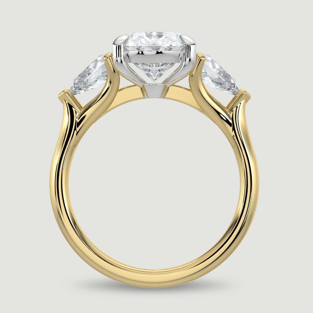 An 18ct yellow gold three stone diamond engagement ring, set with a lab-grown oval shape diamond centre stone held in a platinum four claw setting flanked by a pear shaped lab-grown diamond on either side, held in three claws. Viewed from the side.