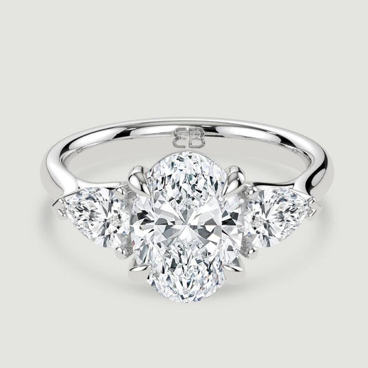 A platinum three stone diamond engagement ring, set with a lab-grown oval shape diamond centre stone held in a four claw setting flanked by a pear shaped lab-grown diamond on either side, held in three claws. Viewed from above.