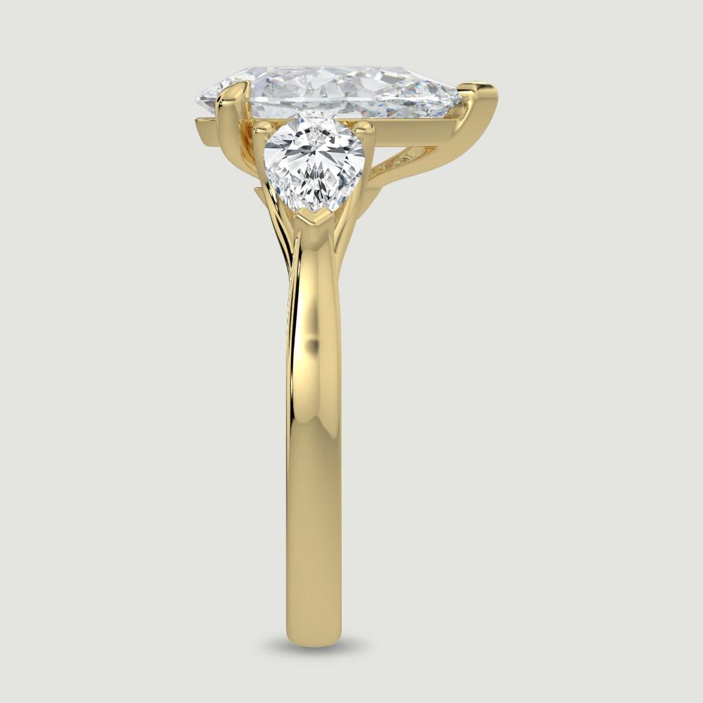 An 18ct yellow gold three stone diamond engagement ring, set with a lab-grown pear shape diamond centre stone held in a three claw setting flanked by a pear shaped lab-grown diamond on either side, held in three claws. Viewed from the edge.