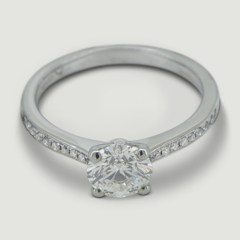 Platinum diamond engagement ring set with a round diamond in a four claw setting with grain set shoulder stones - view from an angle