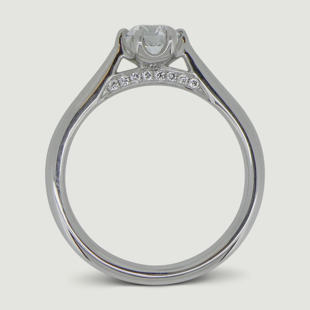 Platinum solitaire engagement Ring. The main Round diamond is held in a six claw crucible setting that sits atop a grain set diamond bridge - view from the side