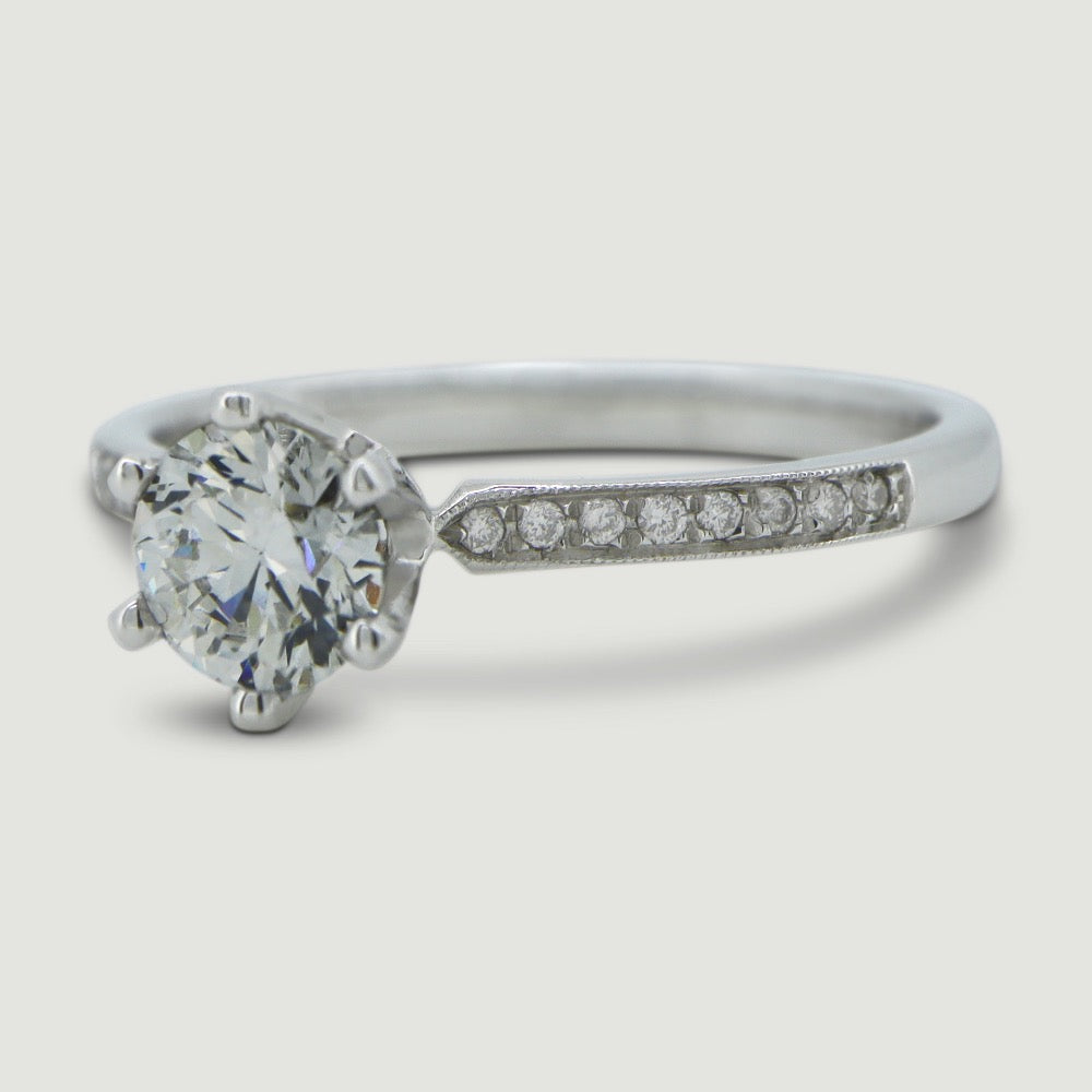 Platinum solitaire engagement Ring. The main Round diamond is held in a six claw Tiffany-style setting with diamonds grain set half way down the shoulders - focus on the shoulder stones